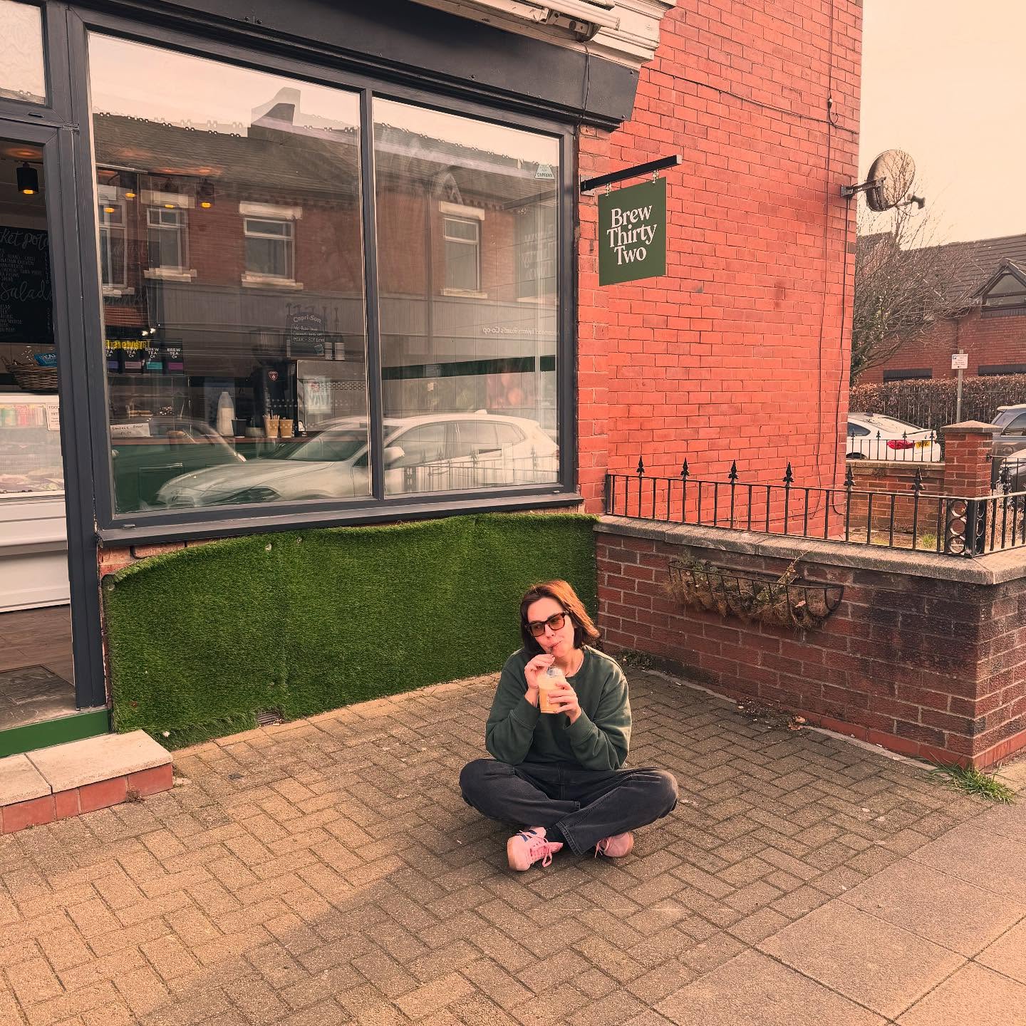 Photo of the Brew Thirty Two shopfront, showing a green door, and hand painted shop sign