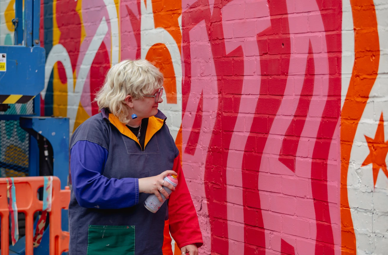 Photo of Becky looking at her spray painted mural, incorporating bright colours and bold typography